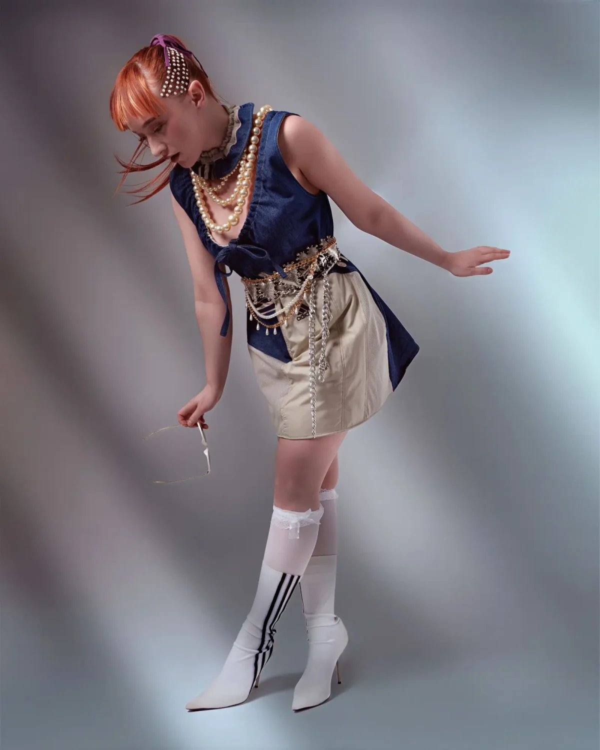 Editorial fashion portrait featuring copper hair, pearl accessories and layered sports-luxe styling with white heeled boots.