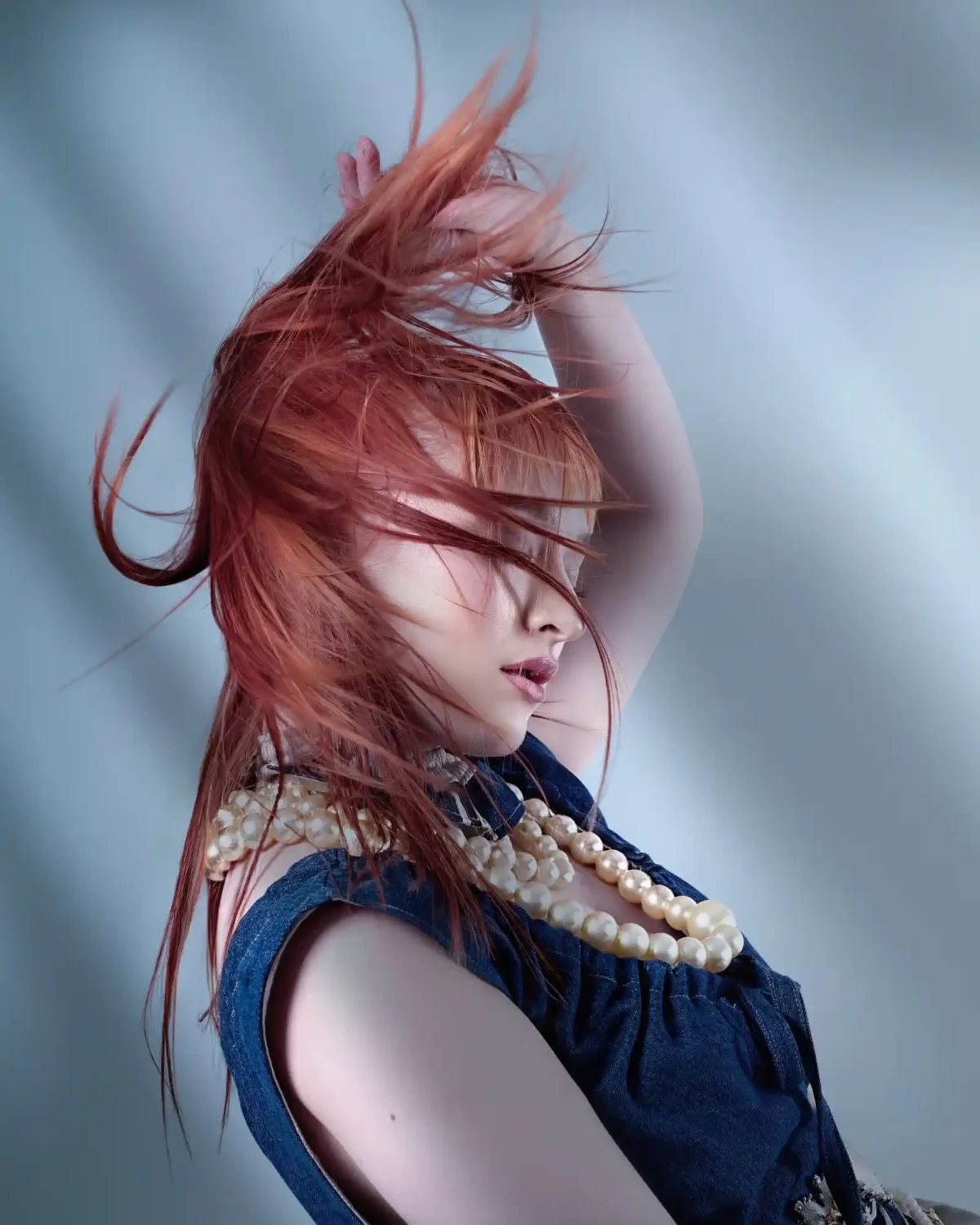 Editorial portrait featuring copper-red textured hair swept across the face with pearl accessories and flowing movement.