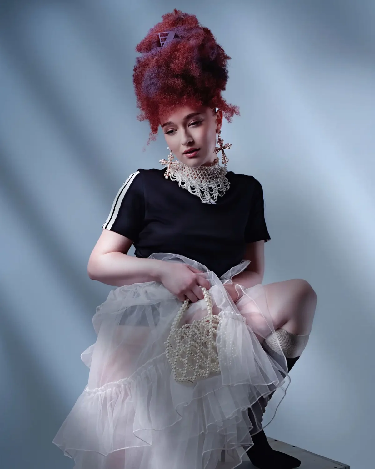Editorial portrait featuring a voluminous textured updo with rich red tones, paired with layered tulle and pearl accessories.