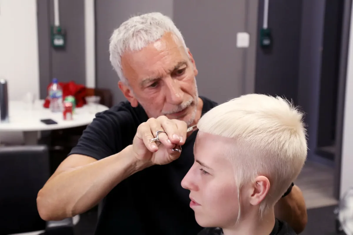 Hairdresser Akin Konizi cutting a client’s platinum blonde pixie crop during a salon session.