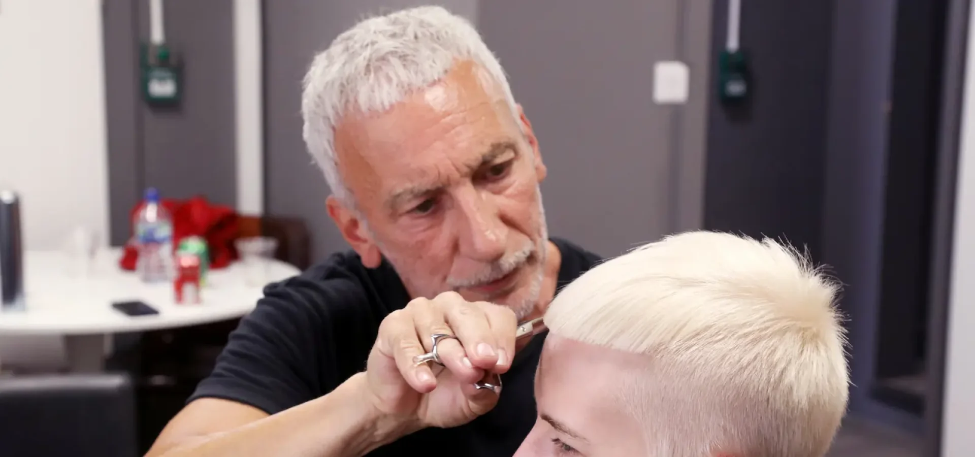 Hairdresser Akin Konizi cutting a client’s platinum blonde pixie crop during a salon session.