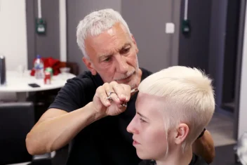 Hairdresser Akin Konizi cutting a client’s platinum blonde pixie crop during a salon session.