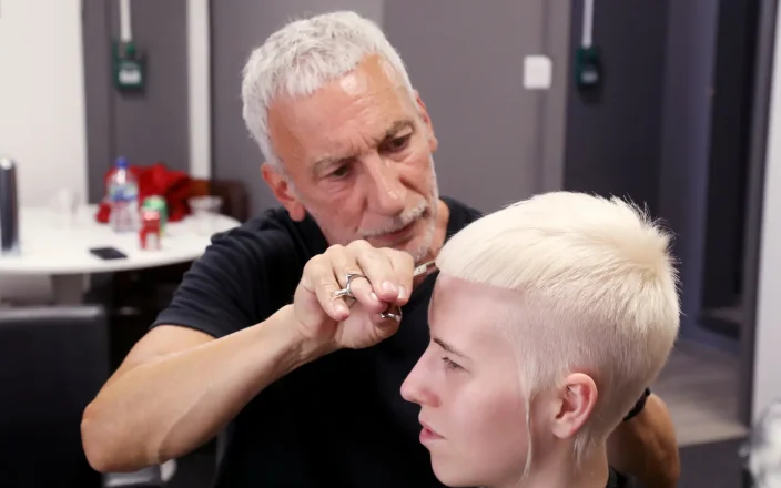 Hairdresser Akin Konizi cutting a client’s platinum blonde pixie crop during a salon session.