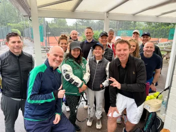 Group of tennis players and Hair & Beauty Charity supporters posing courtside during a charity fundraising tournament.