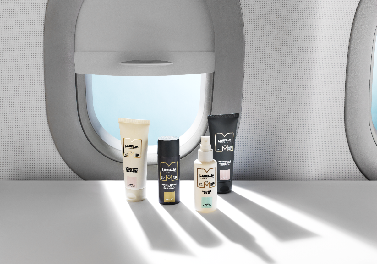 LABEL.M travel-sized haircare products displayed on an airplane tray table beside an aircraft window.