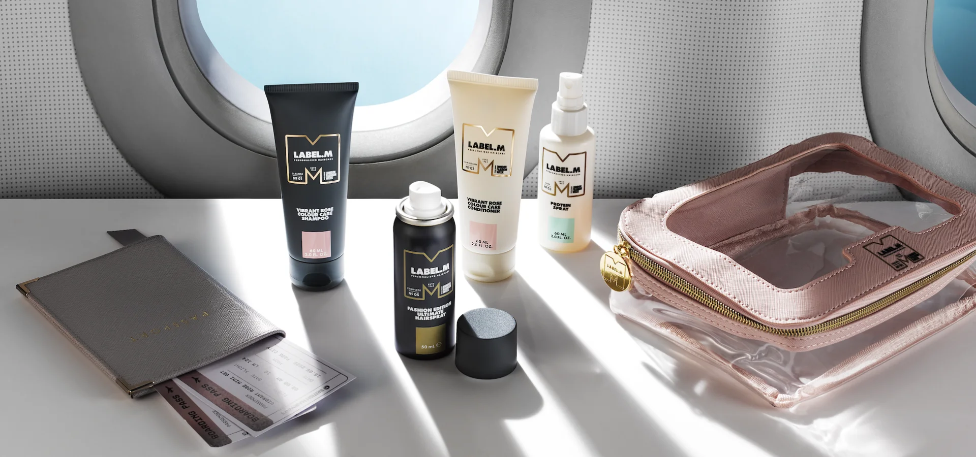 LABEL.M mini haircare collection displayed with travel essentials beside an airplane window.