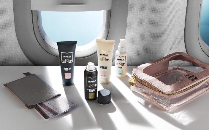 LABEL.M mini haircare collection displayed with travel essentials beside an airplane window.