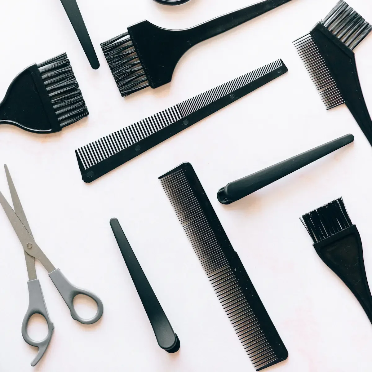 Flat lay of professional hairdressing tools including combs, tint brushes, scissors and styling equipment on white background.