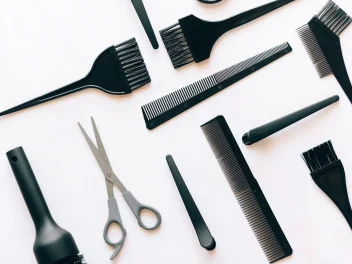 Flat lay of professional hairdressing tools including combs, tint brushes, scissors and styling equipment on white background.