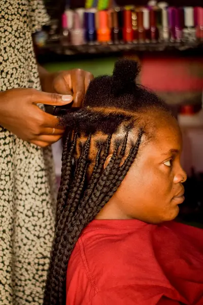 Hair stylist creating neat box braids on client in salon chair with sectioned natural hair and styling tools visible.