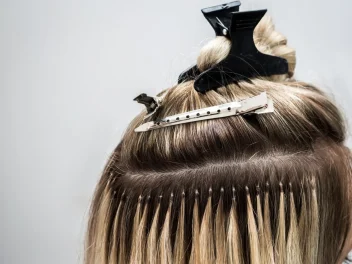 Close-up of blonde hair extensions being applied with sectioning clips and micro bonds during a salon fitting.