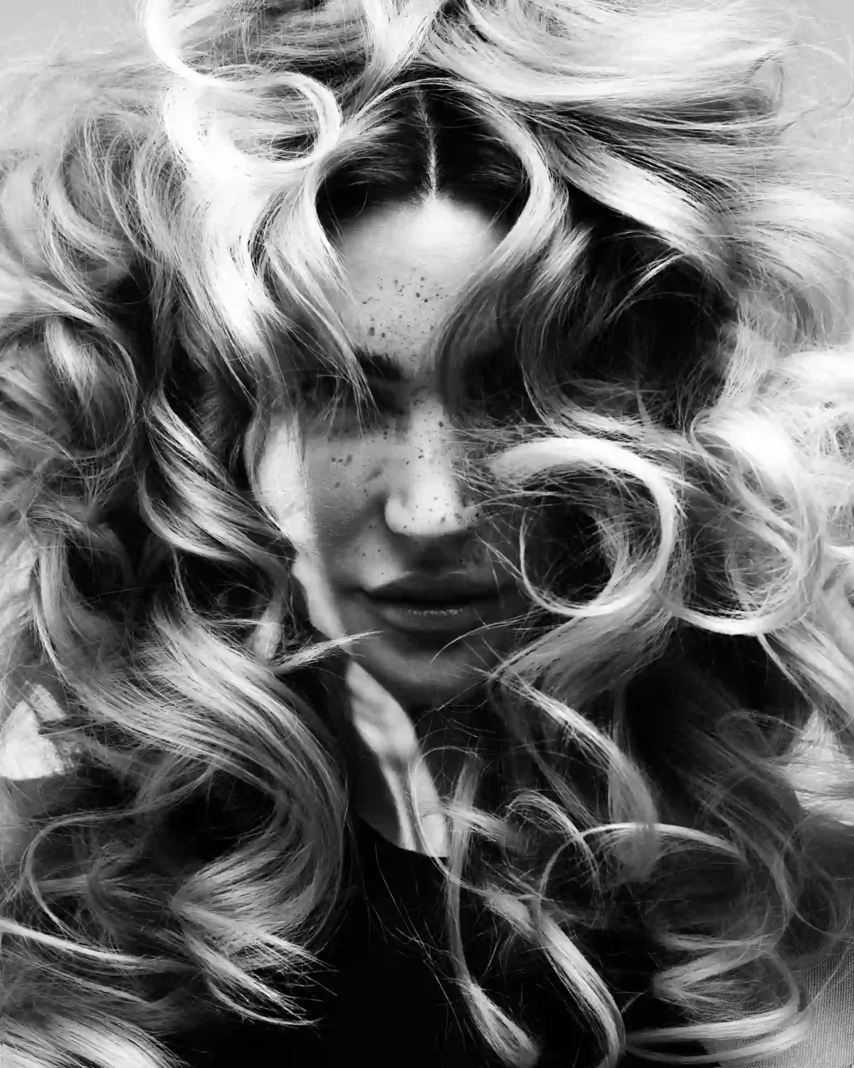 Black-and-white editorial portrait with voluminous curls framing the face and soft texture throughout the hair.