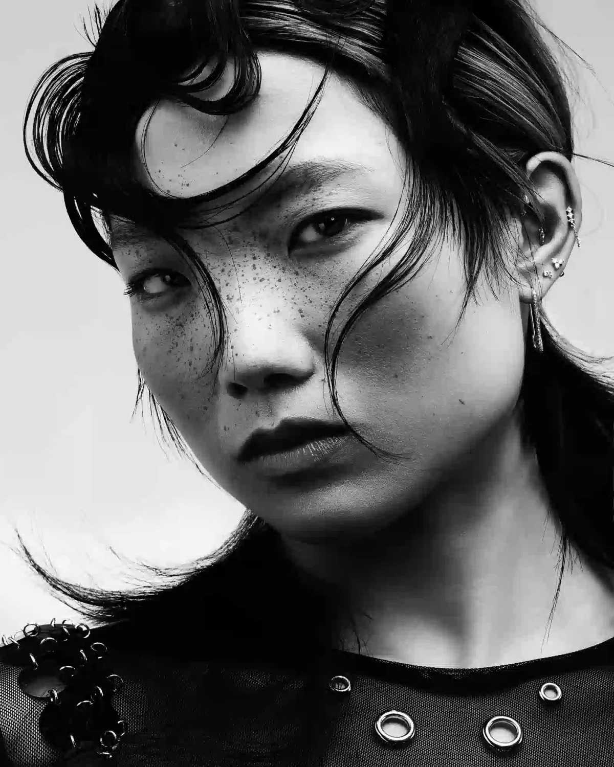 Black-and-white beauty portrait with sculpted wet-look hair, soft curls and textured fringe framing the face.