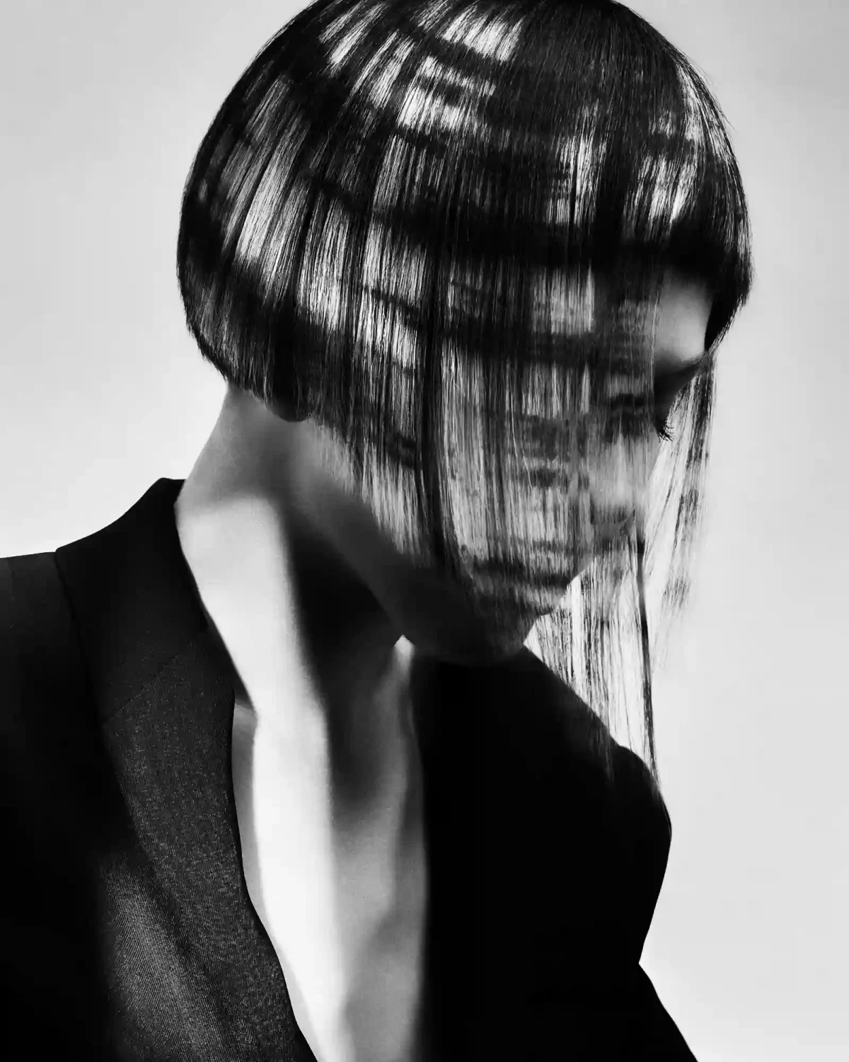Black-and-white editorial bob with glossy precision cut and graphic shadow patterns across the hair and face.
