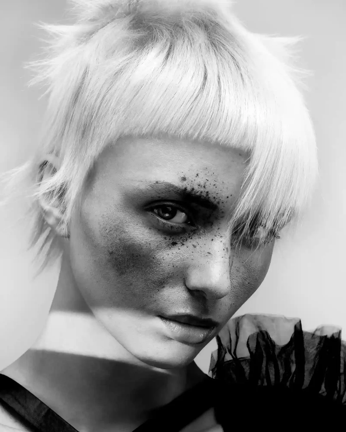 Black-and-white editorial crop with textured fringe, soft layers and dramatic shadowed eye makeup detail.