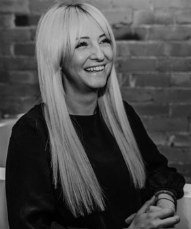 Black-and-white portrait of Sarah Street with long straight hair seated against a brick wall background.