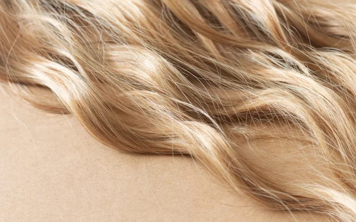 Close-up of glossy blonde beach waves with warm honey tones and soft texture, showcasing healthy, dimensional hair colour.