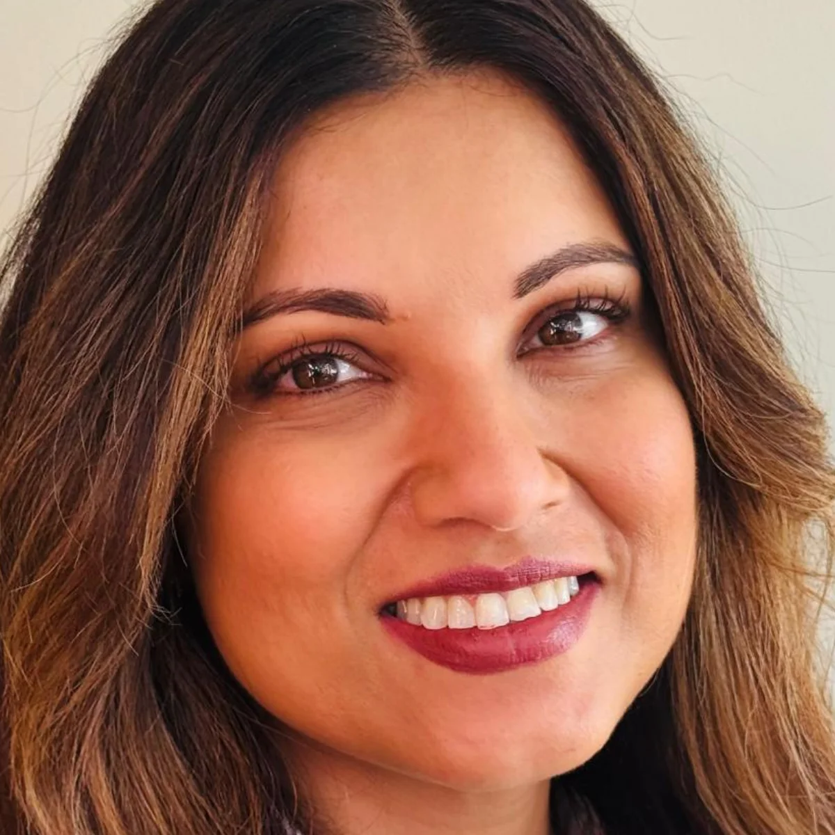 Portrait of Alex Thaddeus, beauty industry professional, smiling with soft waves and natural makeup in a professional headshot.