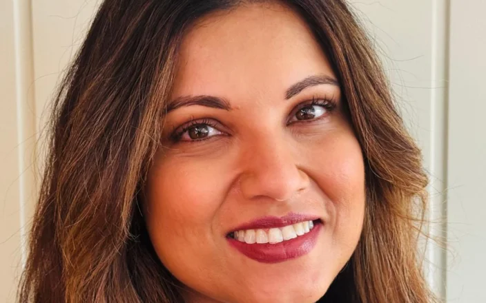 Portrait of Alex Thaddeus, beauty industry professional, smiling with soft waves and natural makeup in a professional headshot.