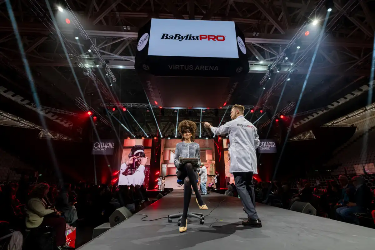 Hairdresser demonstrates on a hair model on stage at the BabylissPRO Legacy show.