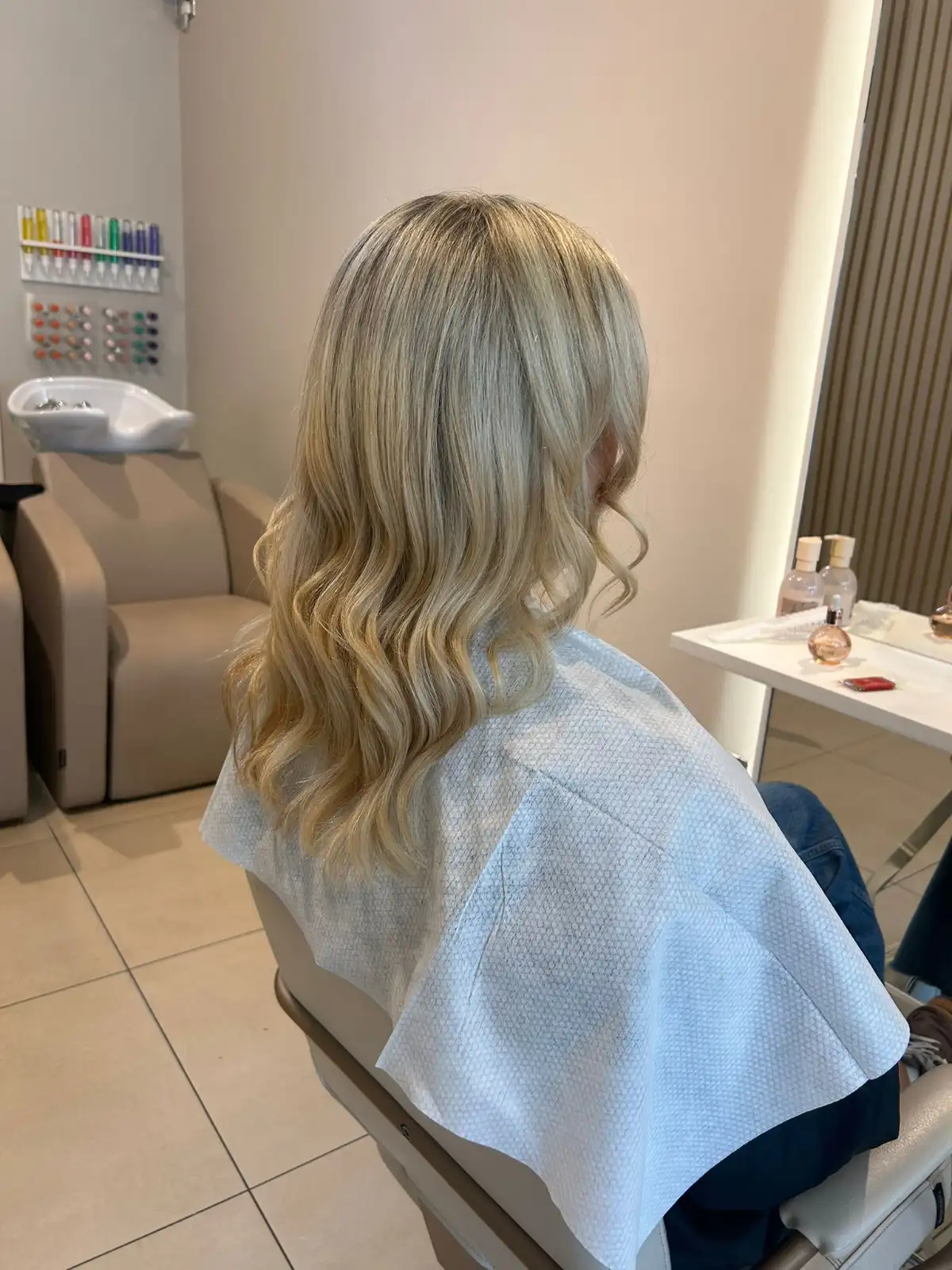 Client with soft blonde waves wearing a disposable salon towel, highlighting a hygienic, eco-conscious and professional salon experience.