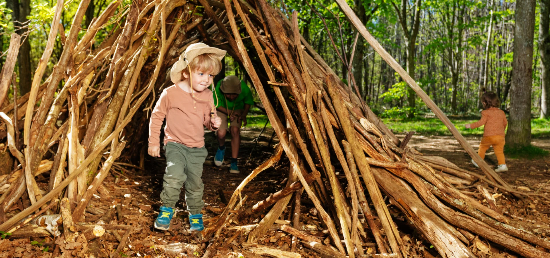Children exploring a handmade woodland den during forest school outdoor learning and nature play activities.