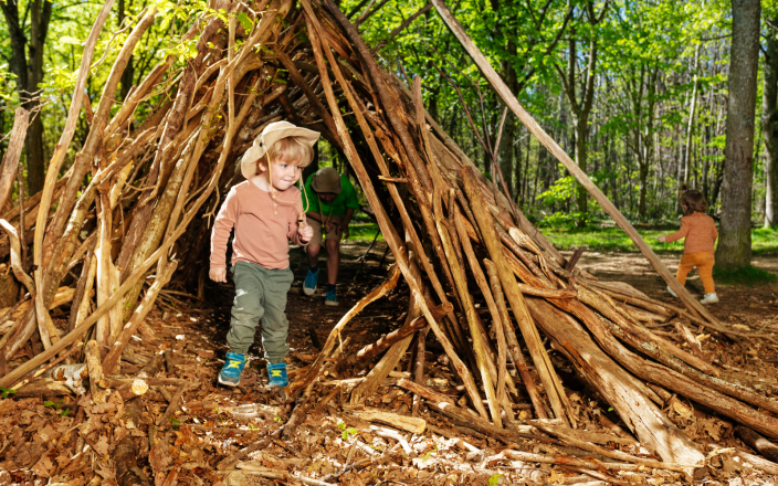Children exploring a handmade woodland den during forest school outdoor learning and nature play activities.