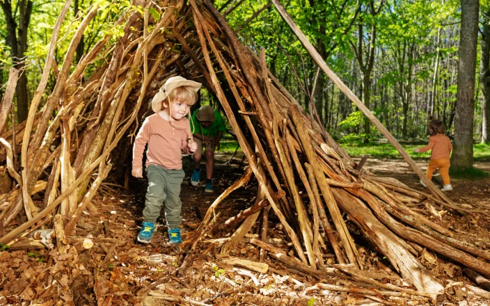 Children exploring a handmade woodland den during forest school outdoor learning and nature play activities.