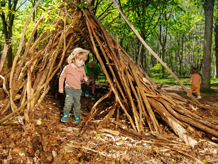 Children exploring a handmade woodland den during forest school outdoor learning and nature play activities.