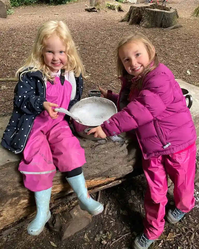 Children enjoying outdoor forest school activities while mixing mud in a woodland play area during nature-based learning.