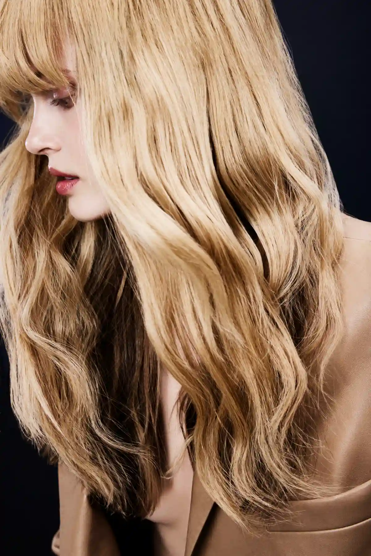 Model with soft golden blonde waves and seamless dimension, showcasing healthy summer hair with natural movement and shine.