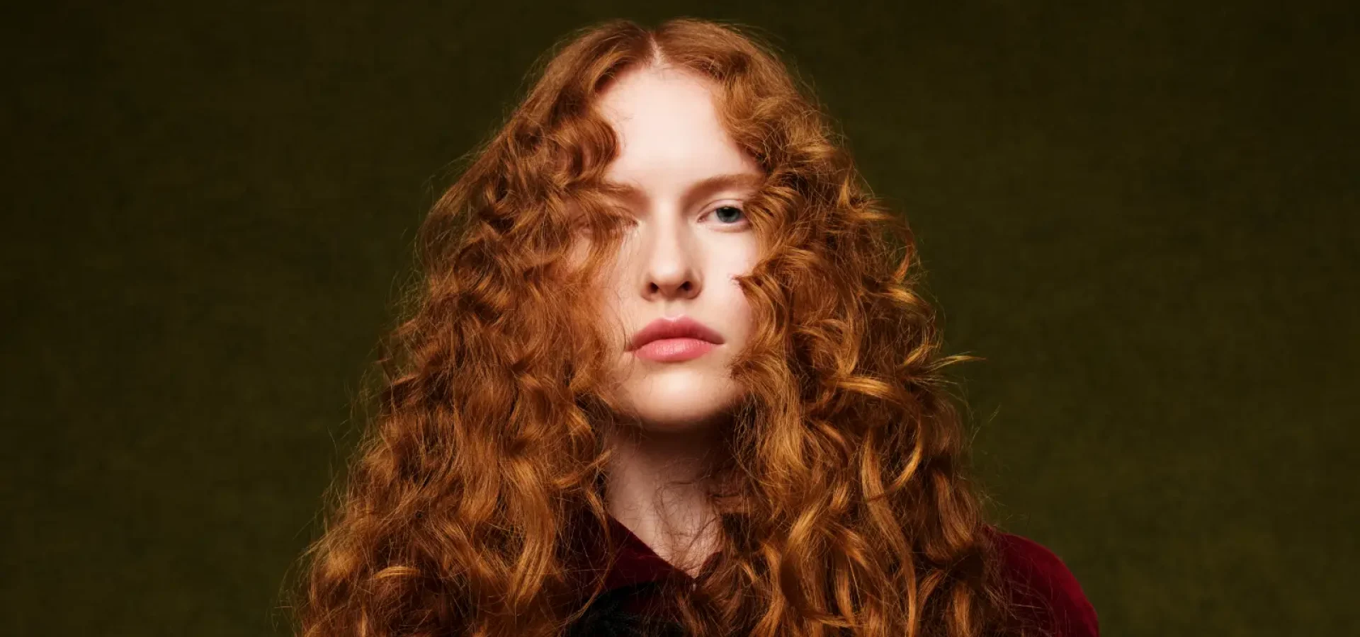 Fashion portrait featuring long, voluminous copper curls inspired by 80s hair trends, styled with texture, movement and editorial flair.