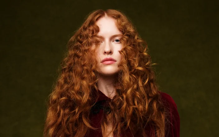 Fashion portrait featuring long, voluminous copper curls inspired by 80s hair trends, styled with texture, movement and editorial flair.