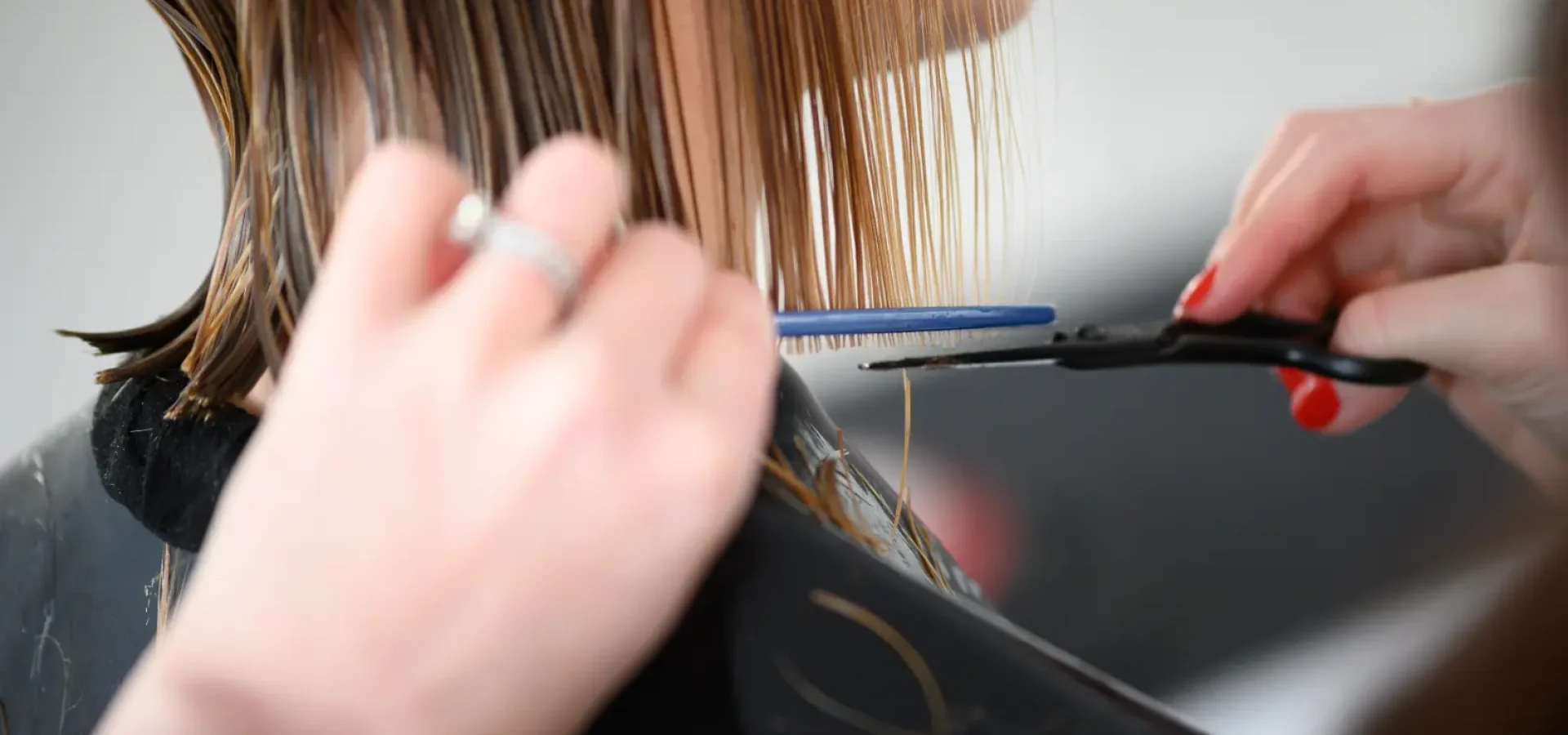 Hairdresser trimming wet blonde hair with scissors and comb during a precision salon haircut appointment.