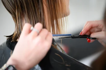 Hairdresser trimming wet blonde hair with scissors and comb during a precision salon haircut appointment.