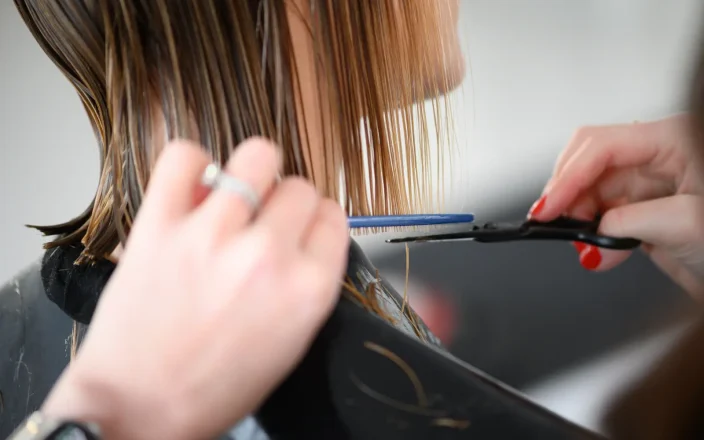 Hairdresser trimming wet blonde hair with scissors and comb during a precision salon haircut appointment.