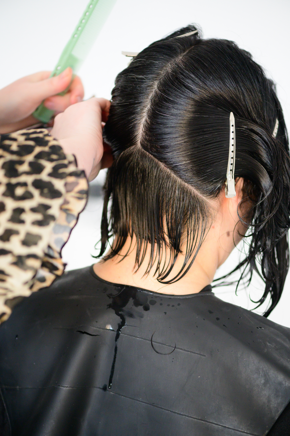 Hairdresser sectioning wet black hair with clips during a precision haircut in a professional salon setting.