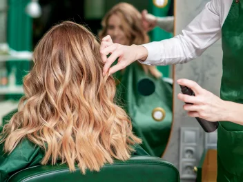 Stylist creating soft blonde waves with finishing spray during a salon hair styling appointment.