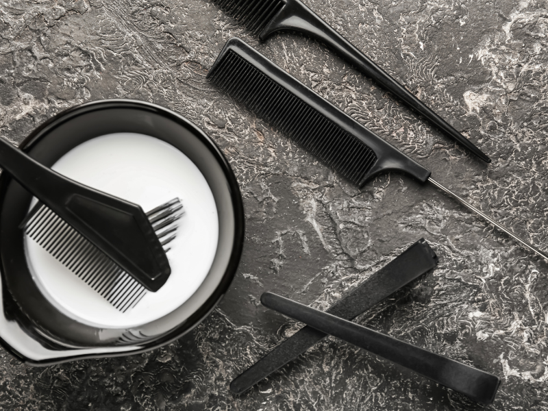 Hair colouring tools with tint bowl, brushes and sectioning combs on a salon workstation.