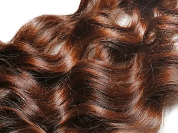 Close-up of glossy copper hair with flowing waves, showcasing rich shine, dimension and healthy texture in a professional salon finish.