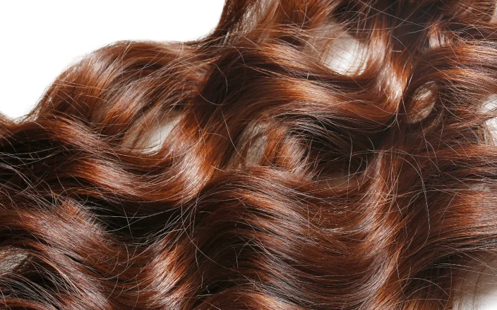 Close-up of glossy copper hair with flowing waves, showcasing rich shine, dimension and healthy texture in a professional salon finish.