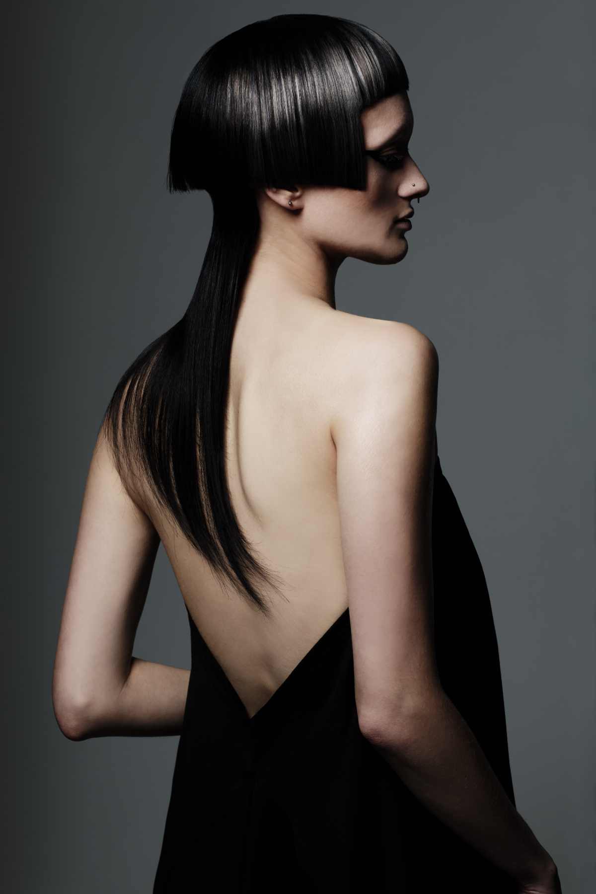 Model with sleek black geometric haircut featuring blunt fringe and long layered back section in editorial styling.