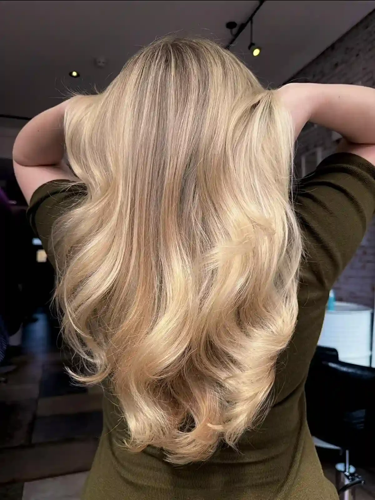 Glossy suede blonde hair with soft layered waves and creamy champagne tones styled in a luxury salon finish.