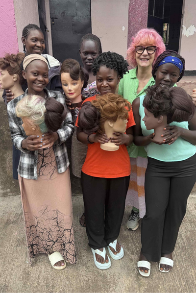 Anne Veck stands with a group of students in Uganda holding mannequin hair models.