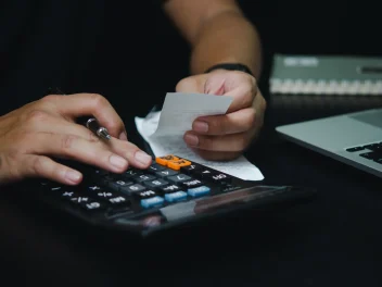 Hairdresser taps at a calculator with once hand, whilst the other hand holds bills and a pen as BHC urges VAT reform.
