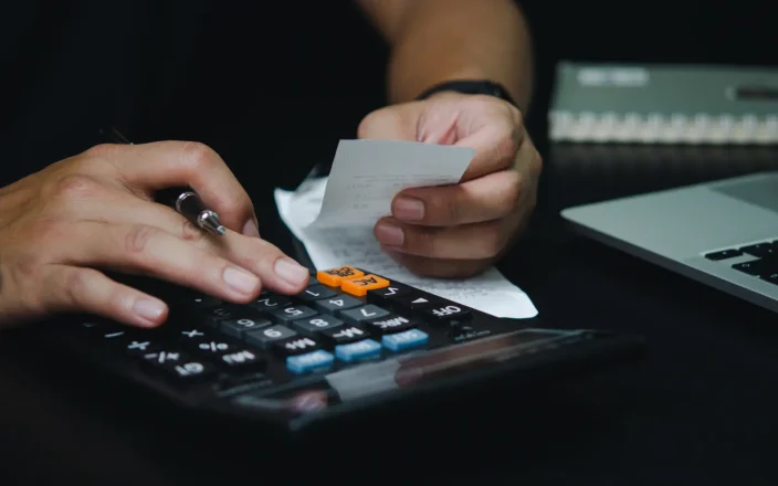 Hairdresser taps at a calculator with once hand, whilst the other hand holds bills and a pen as BHC urges VAT reform.