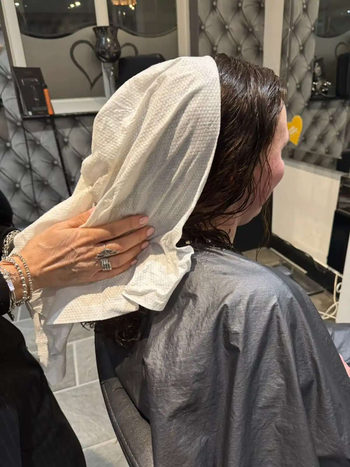 A model sits at a salon's backwash with an Enki Towel on her hair.
