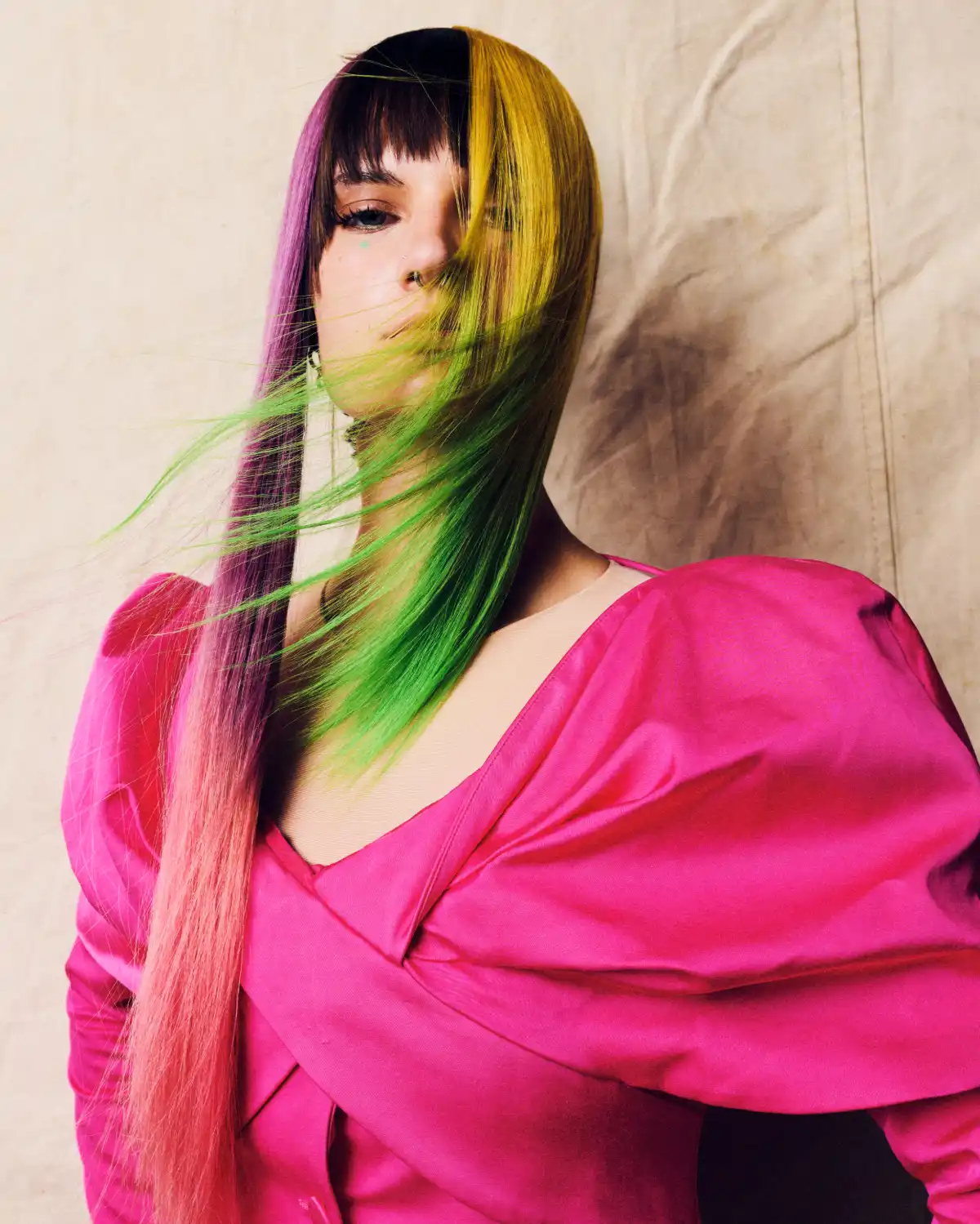 Model with sleek colour-blocked hair in pink, green and yellow tones, styled with a precision fringe for an editorial hair collection.