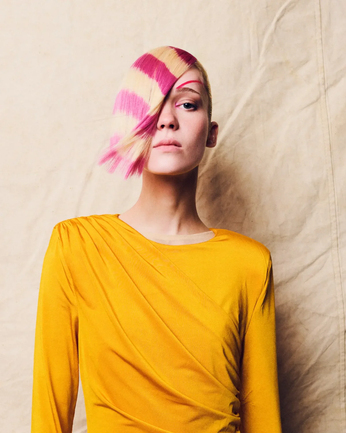 Model with a precision blonde bob featuring bold pink colour blocking and asymmetrical fringe in an editorial hair collection.