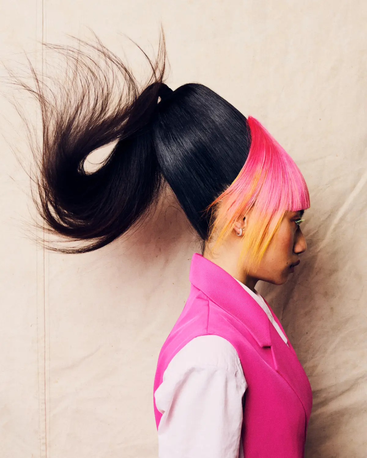 Model with graphic black ponytail, neon pink and orange fringe, and precision cut in a bold editorial hair collection.